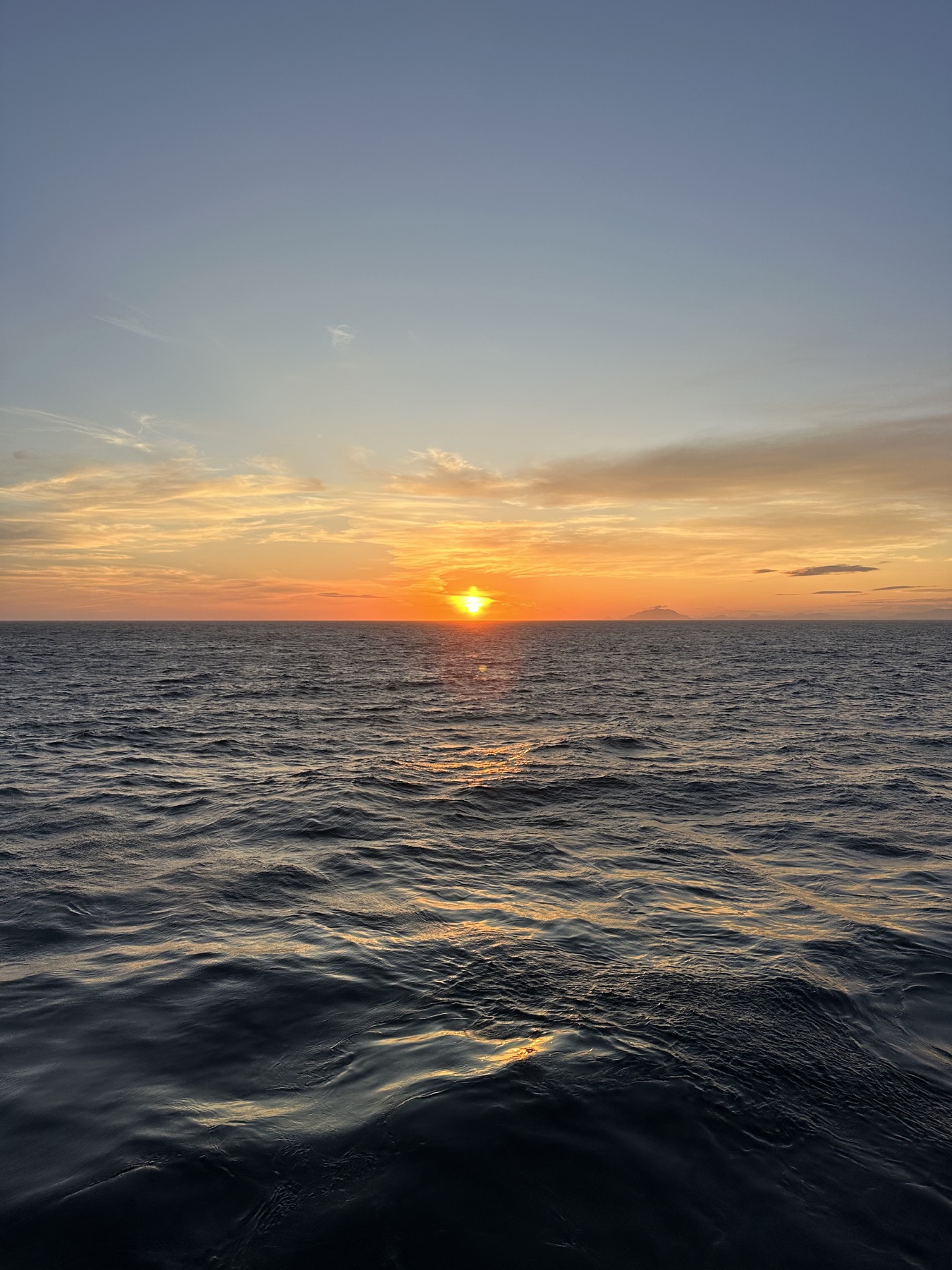 A low sunset over open ocean with dark water in the foreground and a clear horizon.